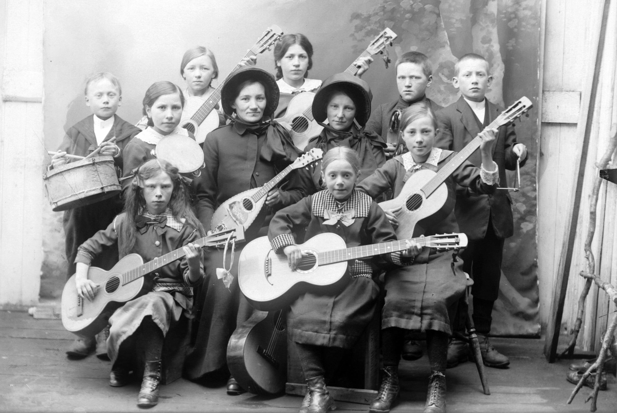 Gruppeportrett av barn og to kvinner med musikkinstrumenter. Kvinnene er trolig med i Frelsesarméen.