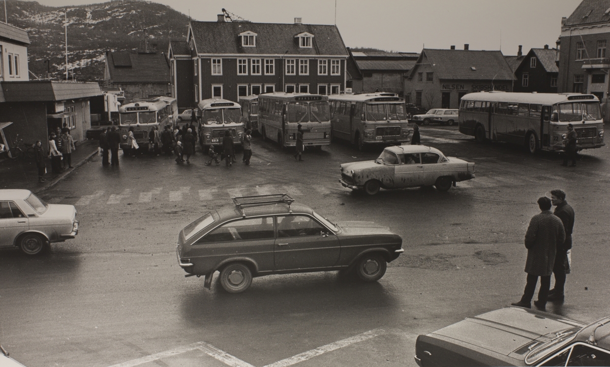 Busser og mennesker på rutebilstasjonen i sentrum, fotografert i 1973 eller 1974. Biltrafikk i forgrunnen.