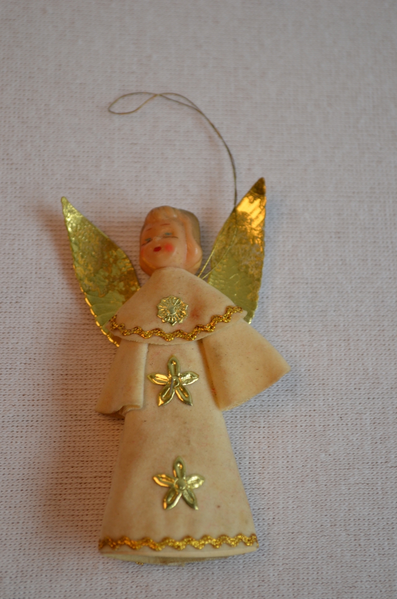 Engel laga av kvitt stoff med gulldekor og vinger av gull. Haudet er av plastikk.