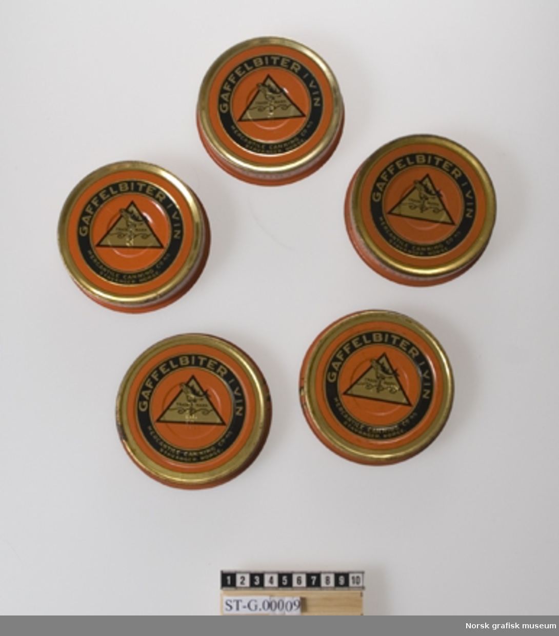 Fem runde hermetikkbokser fra Mercantile Canning Co. A/S. Har inneholdt gaffelbiter i vin. Orange bunnfarge med trykk i sort og gull.