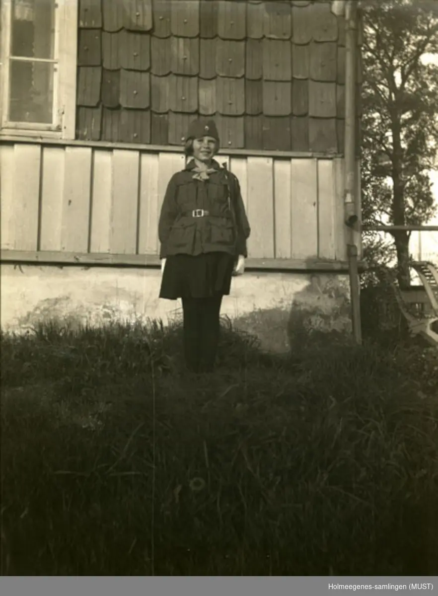 Karen Pedersen i speideruniform, står ved et hjørne av huset på Holmeegenes.