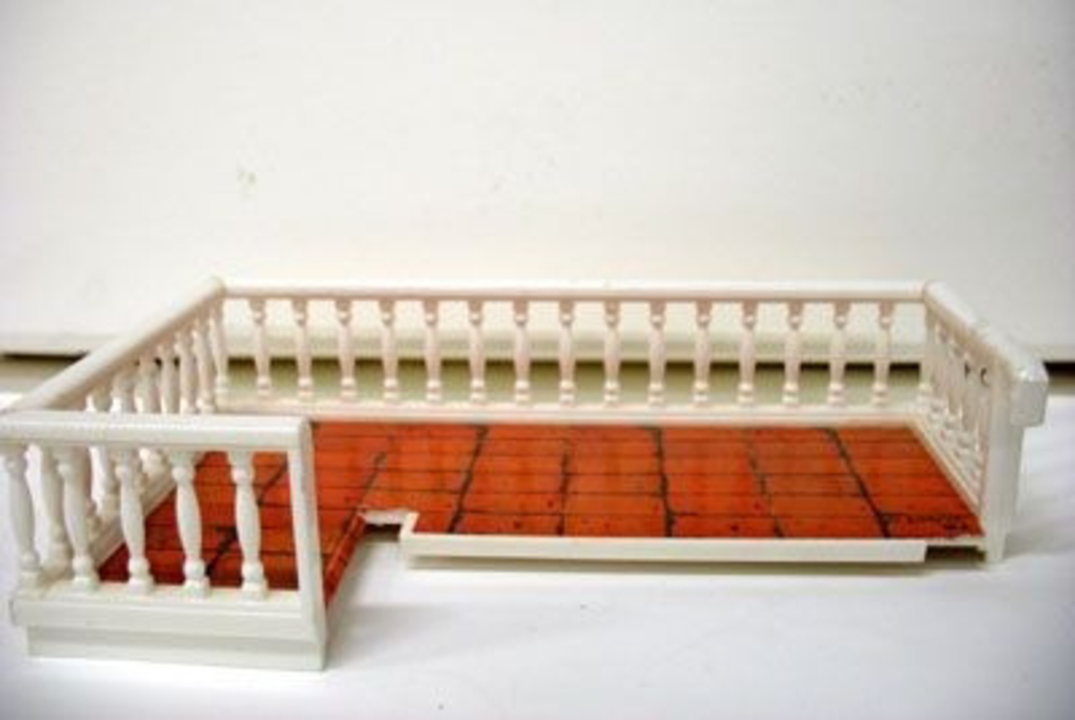 Balkong med vita, svarvade räcken och tegelimitation i papper till golv. Se 21 586:20