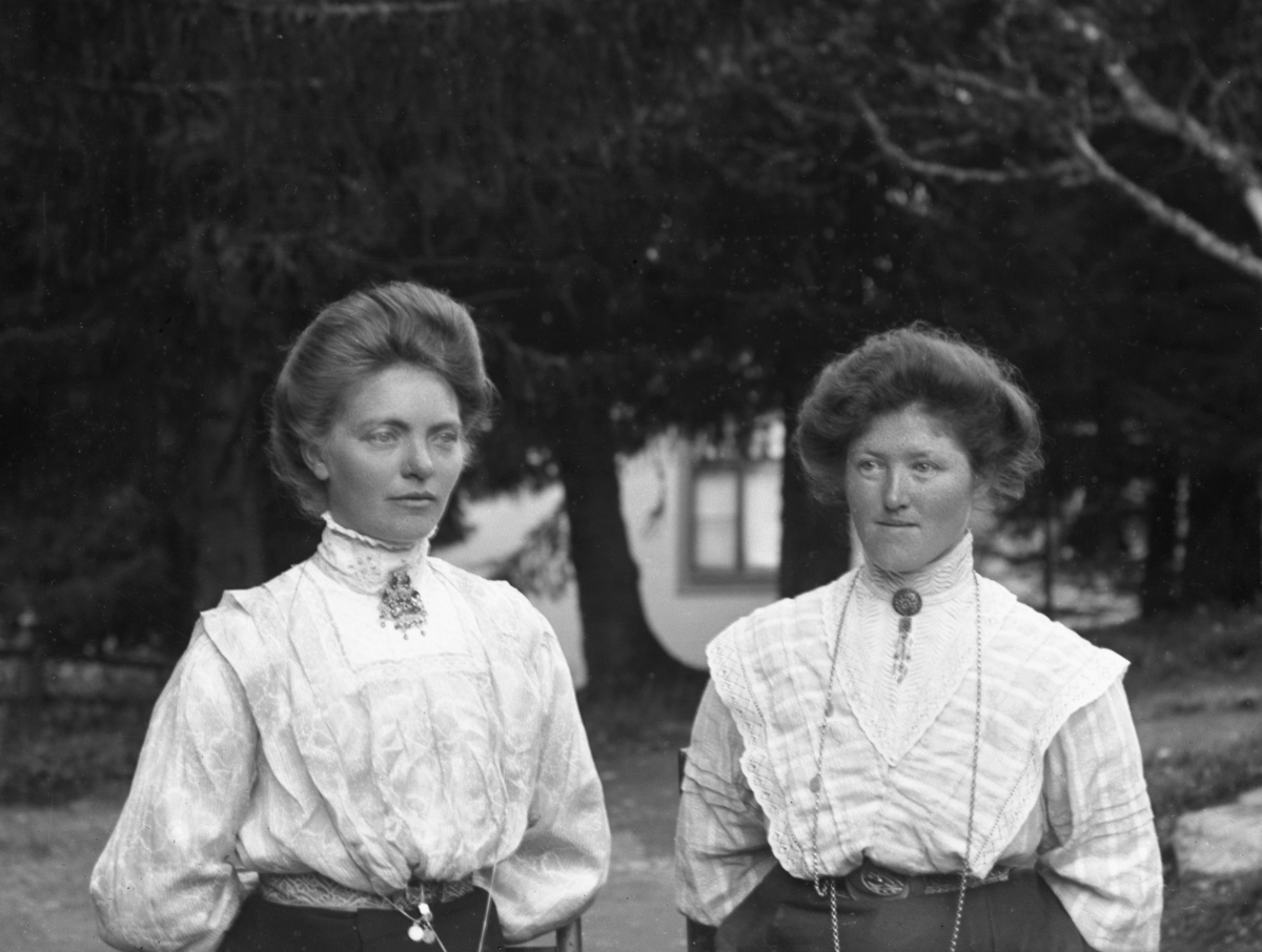 To kvinner kledd i hvite bluser, avbildet på vei, med hus og trær i bakgrunnen