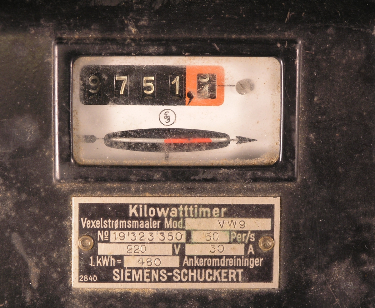 Apparatet har innkast for 1-kronemynter. Det har også en måler som viser kilowatt-timer. Apparatet har hengt på vegg.