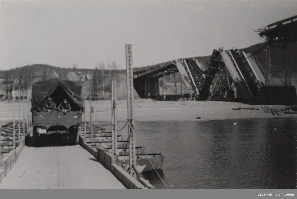 Lastebil kjører over provisorisk bro bygd av den tyske hæren. Den ødelagte Minnesundbroa sees i bakgrunnen.