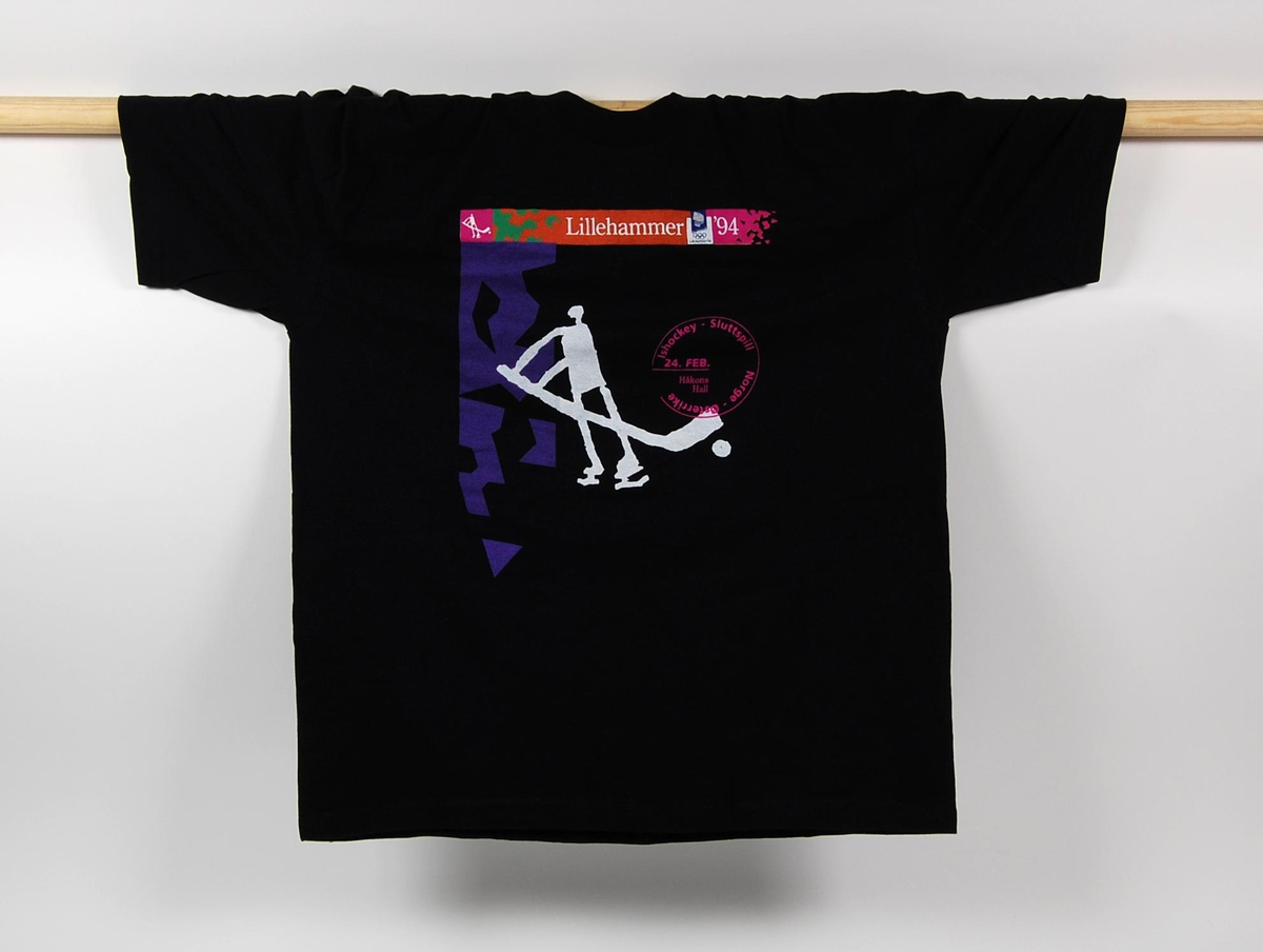 Sort t-skjorte i størrelse XL. T-skjorten har et flerfarget motiv hvor det blant annet inngår et piktogram av en ishockeyspiller. På t-skjorten er det også en logo for de olympiske vinterleker på Lillehammer i 1994.