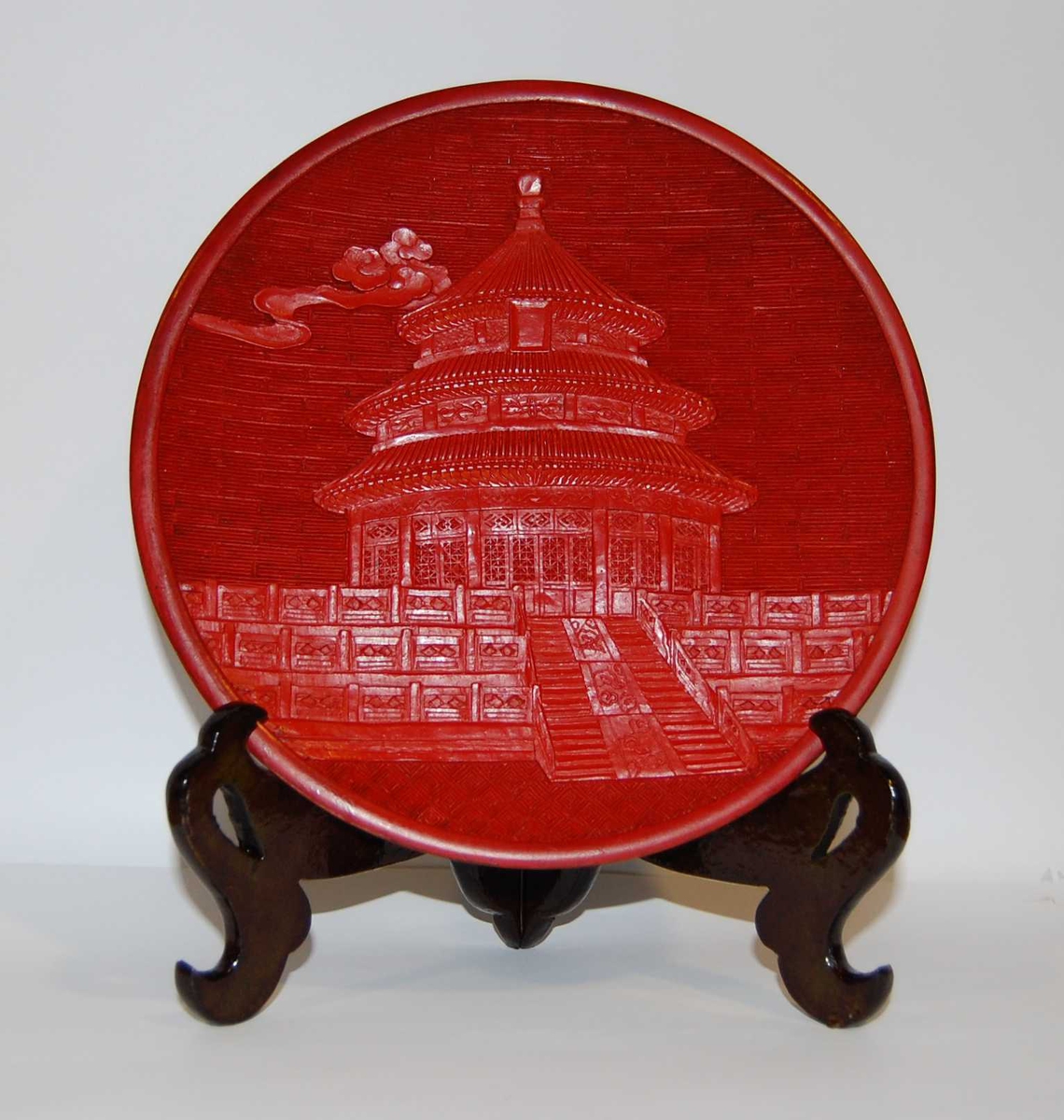 Sort og rød pyntetallerken med motiv av Himmelens tempel i Beijing. Det følger med en støtte til tallerkenen. Tallerkeken ligger i en mønstret eske.