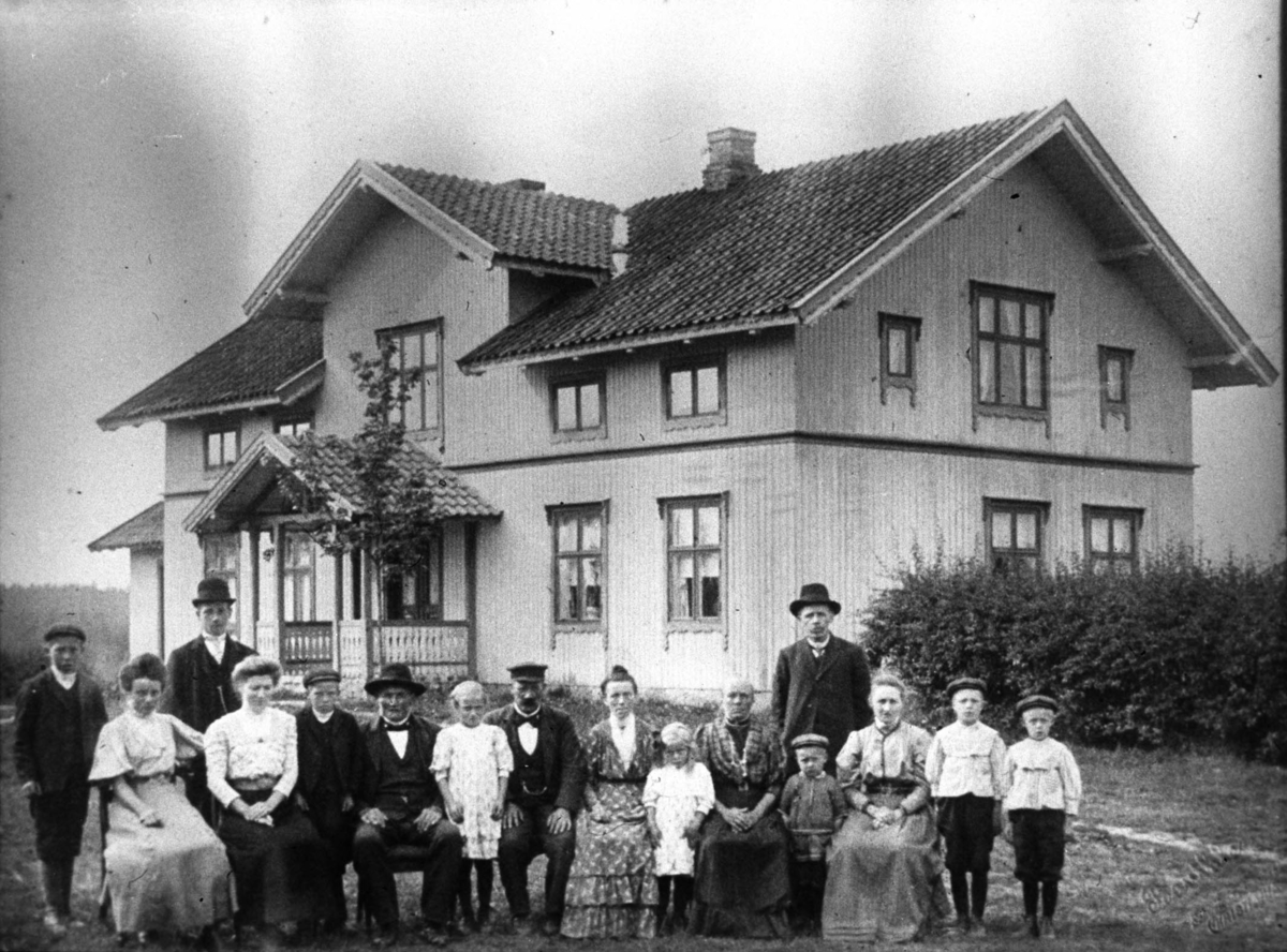 Gruppe med menn, kvinner og barn foran et bolighus.