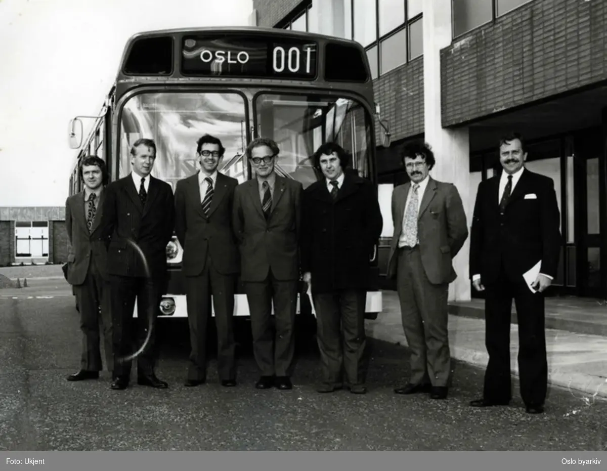 En Leyland National buss. En busstype som ble produsert mellom 1972 og 1985. Da som et samarbeidsprosjekt mellom National Bus Company og British Leyland. Gruppefoto av representanter fra leverandør og mottaker. I midten står ingeniør Orre.