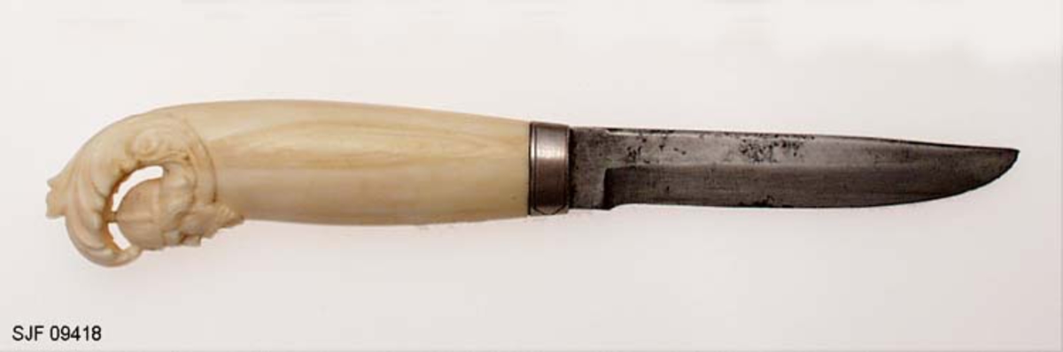 Såkalt «Olavskniv» med skaft av hvalrosstann, skåret av kunsthåndverkeren Lars Prestmoen på Lillehammer. Produksjonen av slike kniver startet han antakelig etter 1930, da det var 1 000-årsjubileum for slaget på Stiklestad i 1030. Knivene ble produsert hos Pipe-Larsen, Lillehammer, hvor Lars Prestmoen da hadde arbeidet i over 40 år.

Kniven er 21,9 centimeter lang, målt fra bladspissen til den bakre enden av knivskaftet. Lengden på knivbladet er 10,2 centimeter. Bladet er snaut 1,9 centimeter bredt ved brystningen, innerst ved skaftet. Tjukkelsen, målt samme sted, er 3,1 millimeter, men bladet smalner framover mot spissen. Bladryggen er slakt konvekst buet. Her er sidekantene, i hvert fall fra et punkt framfor brystningen, avfasete. Bladet har ikke stempelsignatur. Skaftet er lagd av det gulkvite materialet hvalrosstann. Inkludert en cirka 9 millimeter bred sølvholk i den fremre enden er skaftet 11,7 centimeter langt. Den fremre delen er rett, noe konveks i lengderetningen og har et ovalt tverrsnitt. Her er overflata glattpolert. Det fantastiske ved denne kniven er den bakre enden av skaftet, der det ytre skallet er formet som et blad eller ei bølge, som skjermer et mannshode - en mann med skjegg og hjelm - slik Lars Prestmoen forestilte seg den legendariske kongsskikkelsen.

Litt mer informasjon om opphavsmannen til denne kniven finnes under fanen «Opplysninger».