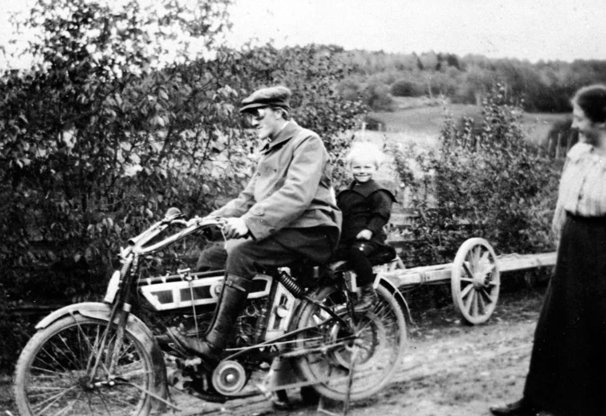 Paul Rogne på motorsykkel på Brøttum, Ringsaker. Gutt bakpå fra Mæhlum nordre. Damen er Ingrid Mæhlum. Motorsykkelen er en europeisk produsert NSU 2 1/2 hk 1913 - 1918