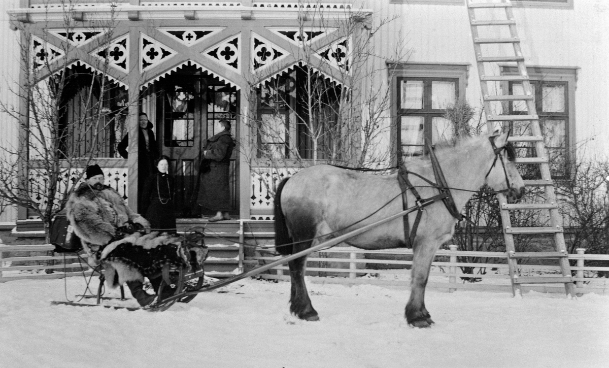 Kjøretur med hest og slede. Mann med ulveskinnspels i sleden. Tre damer ved inngangen på Ulven, Ringsaker. Vinter.
