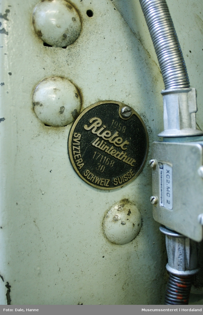Elektrisk ringspinnemaskin (1958) frå det sveitsiske selskapet Rieter. Øvst på maskina plasserer ein spolane med forgarn frå kardemaskina. Reint teknisk er det tre hovudelement i spinninga:  forgarnet blir strukke, tvista (snodd) for å få meir styrke, før det ferdige garnet blir oppvikla på ein spole eller 'spinnepipe'. Tråden går under eit transporthjul i tre, gjennom støypte løpegangar og vidare nedover: Garnet blir snodd ved at garnet passerer ein løpar som beveger seg på ein ring, før det blir samla på ein sylindrisk metallspole. Det er ei rekkje små støvsugarar langs heile maskina, små røyr som stikk ut over spolane. Desse syg til seg støv og/eller tråden viss den ryk, for å unngå at den kjem inn i maskina. Trådrestar og støv blir samla opp i eit oppsamlingskammer på venstre sida av maskina. Der er det òg ein målar som måler kor mykje maskina spinner.

Drivverket og ein stjernemotor sit på høgre sida av maskina. På sida står det "Rieter" i raudt, og det er to målarar som måler omdreiingar/hastigheit på maskina. Det er ei rekkje med 136 koner på kvar side. Maskina kan byggjast på i seksjonar, og slik utvidast etter behov, noko som er vanleg for spinne- og spolemaskiner.