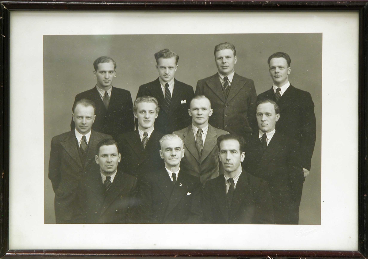 Gruppebilde, innendørs, av 11 velkledde menn stående.Skipsførerskolen 1944-45.
