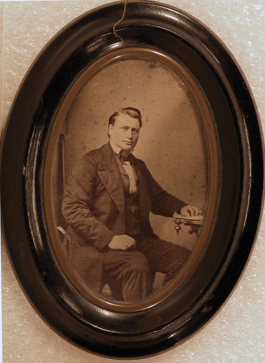 Portrett av finkledd mann sittende på stol ved et bord.