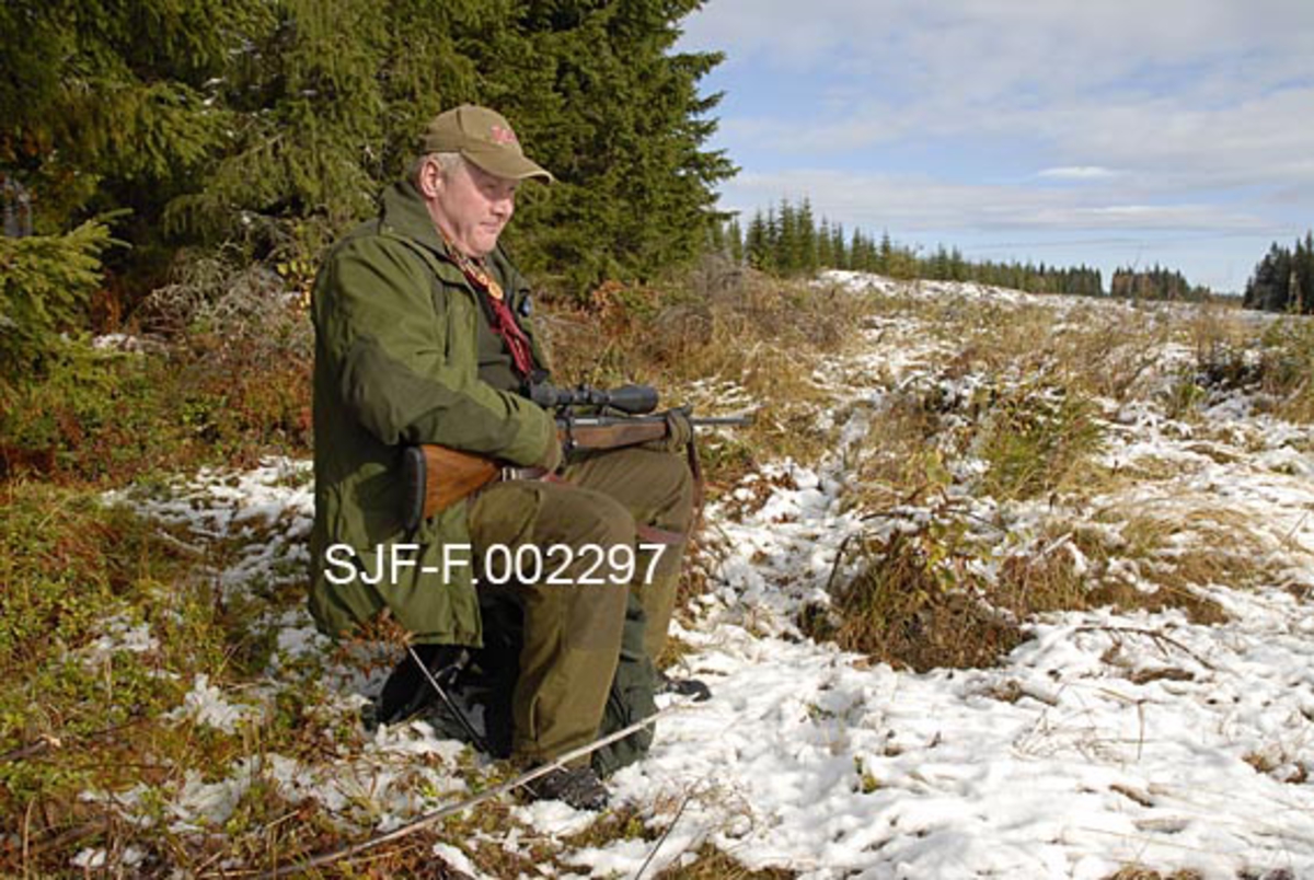 Elgjeger Arnt Svendsberget sitter på elgpost i Tørråsen i Åmot, Hedmark. Bildet ble tatt under elgjakta i 2009.  Jegeren hadde valgt en posisjon i utkanten av ei åpen flate, med granskog bak seg og åpent lende foran og sidevegs.  Han satt på en kappstol med våpenet i fanget.