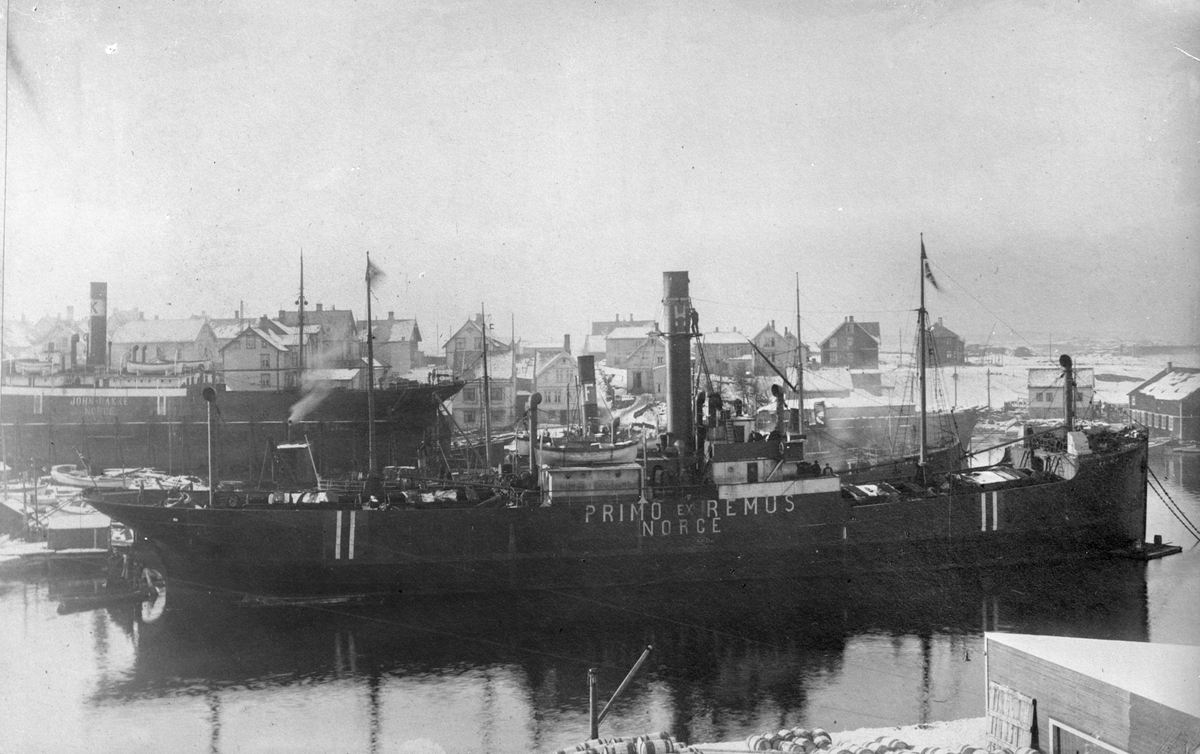 Dampskipet D/S "Primo" ankret opp  ved Smedasundet in Haugesund. Trehus, stort skp og mindre båter i bakgrunnen.