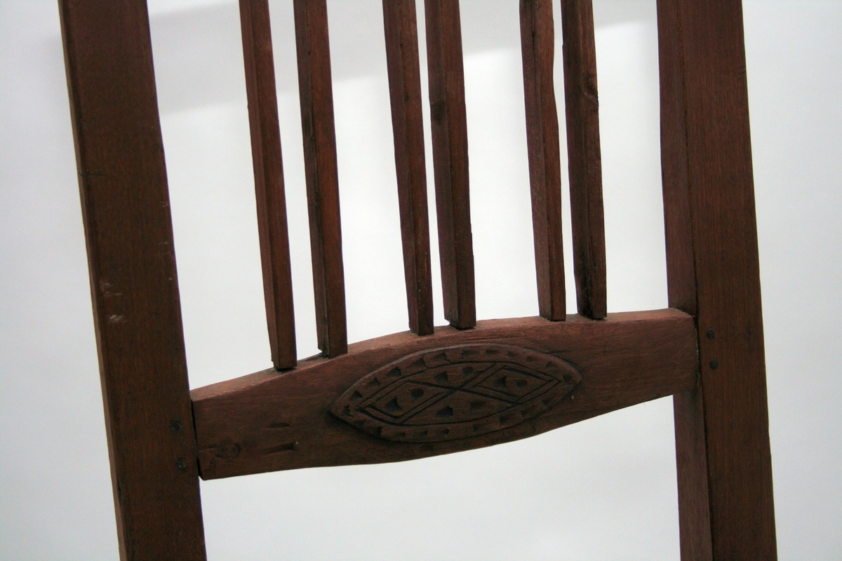 Rødmalt stol med 6 dobbeltstilte vertikale spiler i ryggen, og utskåret oval i horisontal ryggspile. 
En av to like stoler.
