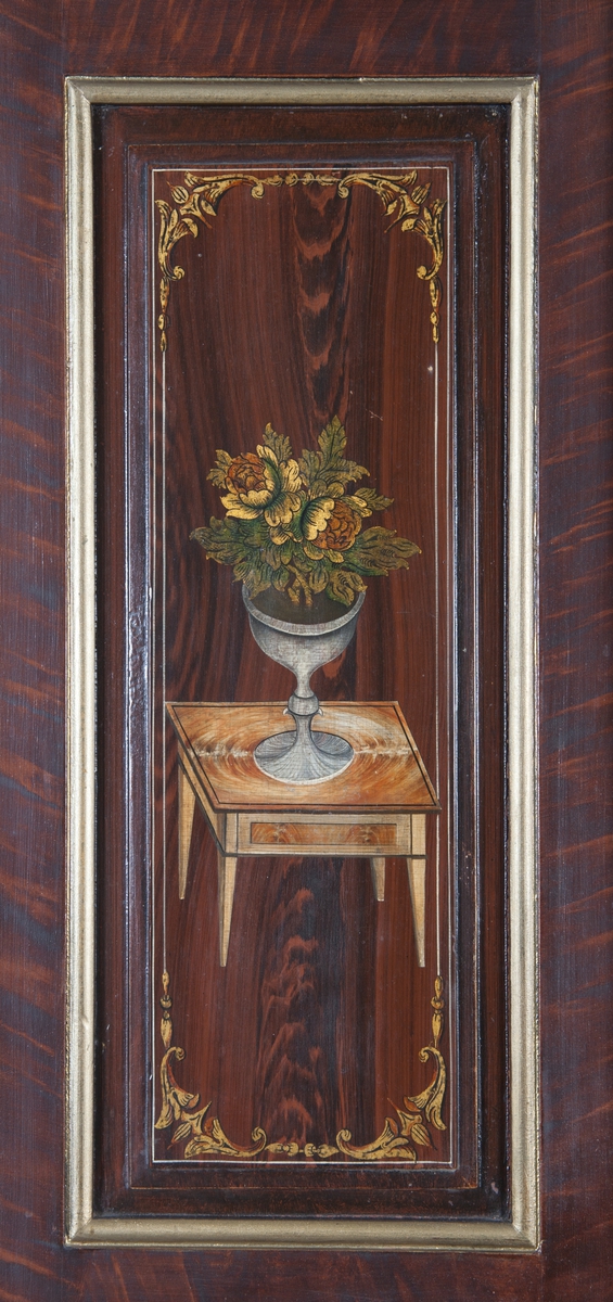 Hjørneskap i to deler. Gullmalte profillister og rosamalt inni. Skapsdørene på overskapet er dekorert med samme motiv på begge dørene, et bord med en vase med blomster.