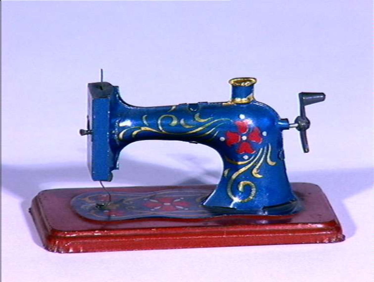 Dukkehus inventar, symaskin, i blikk malt blå og rød med blomsterdekor.