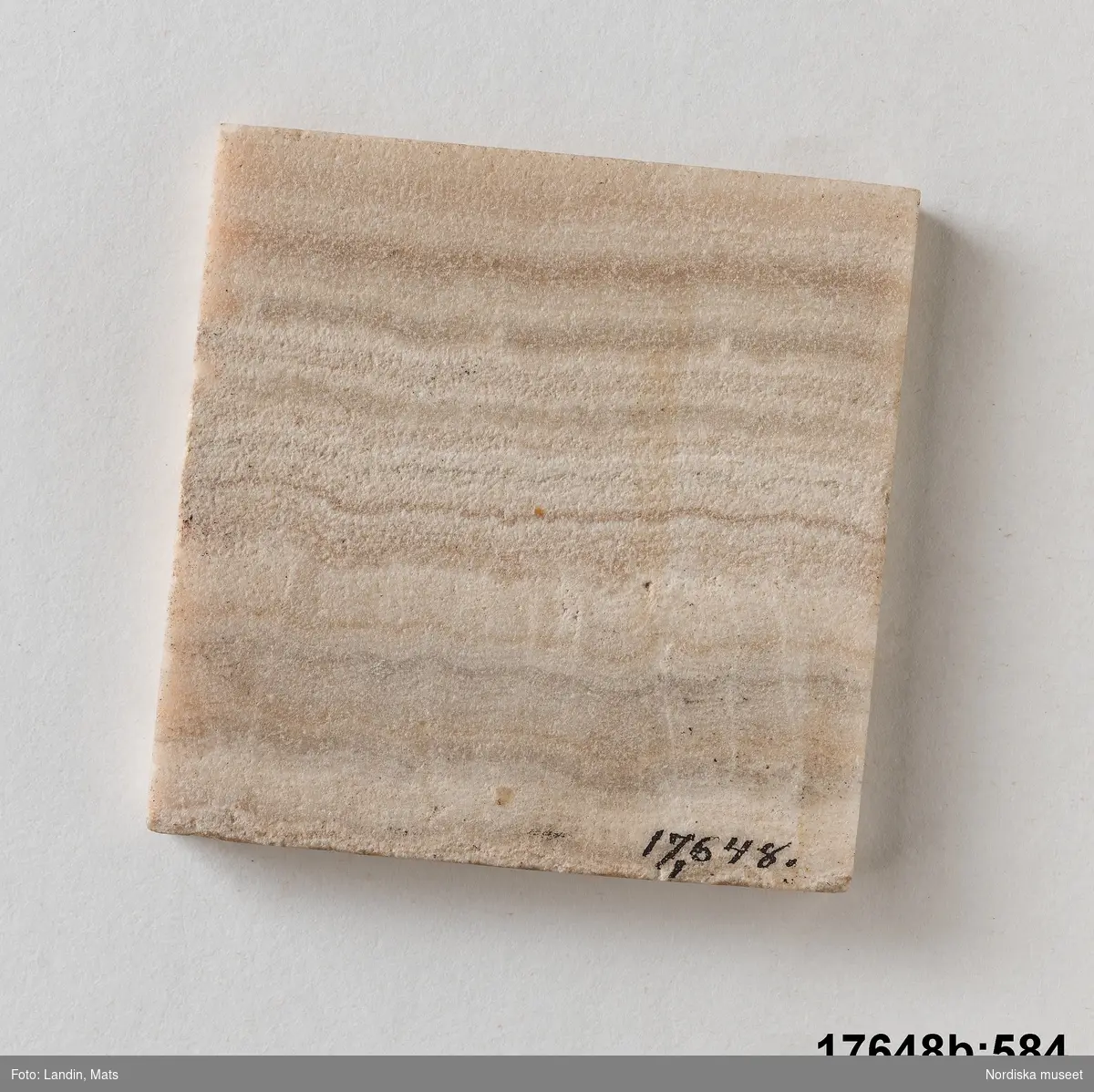 Kvadratisk platta av sten (trol. alabaster). Randigt mönster i olika bruna och vita nyanser. 
/Leif Wallin 2014-01-07