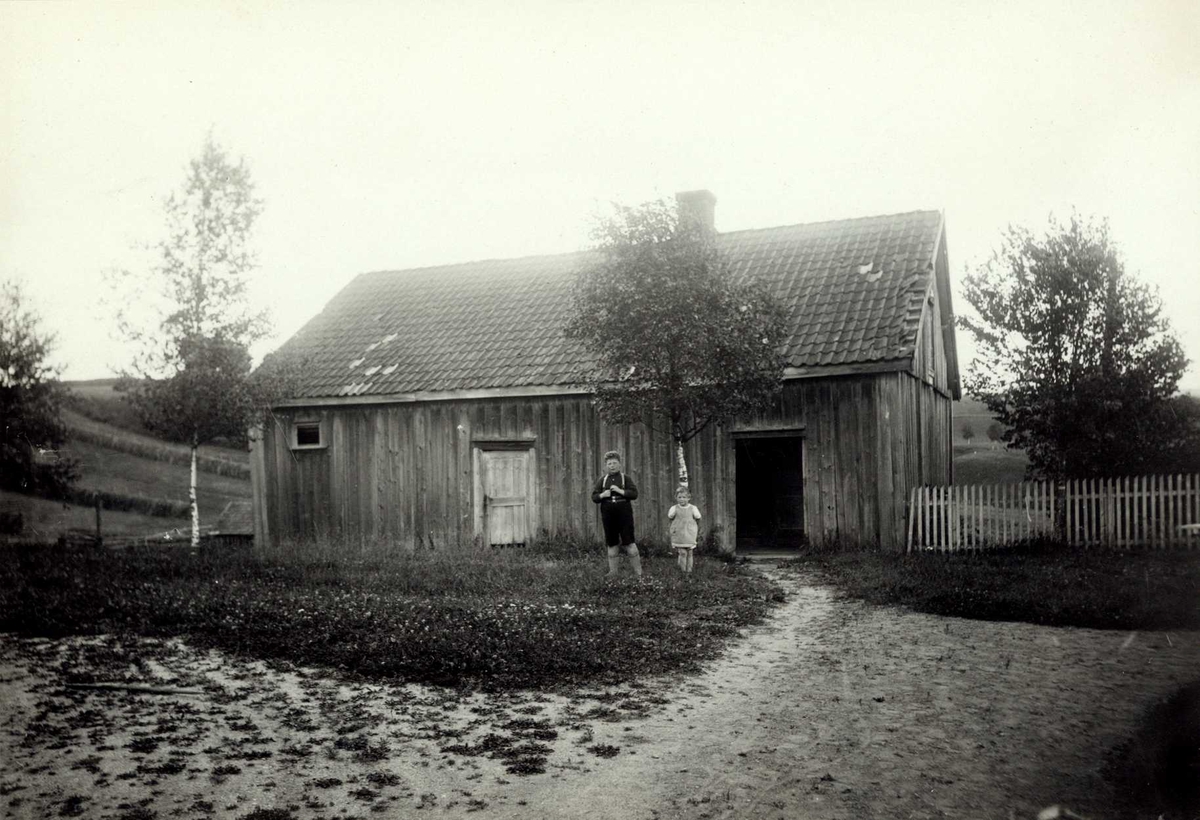 Blosa, Fet, Nedre Romerike, Akershus. Gårdsplass med to barn foran uthus.