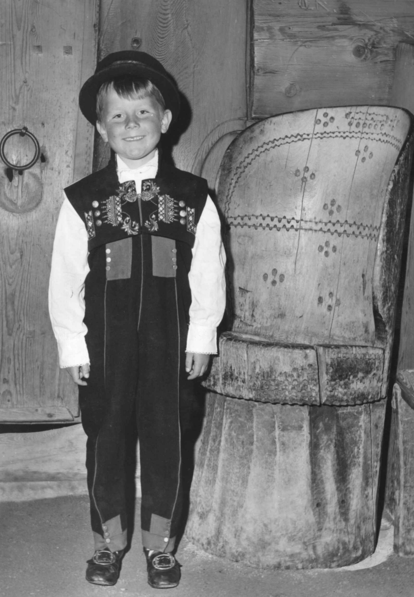 Gutt i folkedrakt står ved kubbestol. Opptreden av Norsk Folkemuseums barneleikarring.