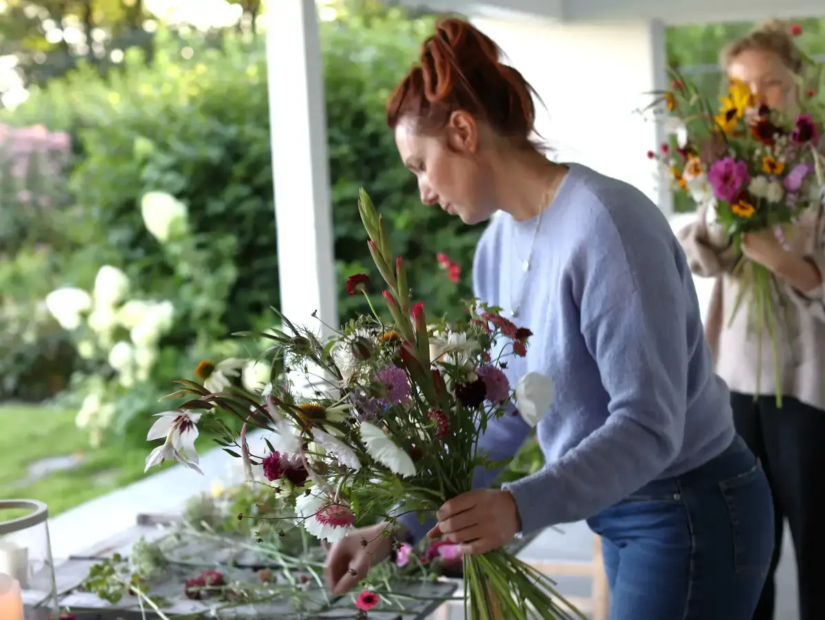 Foto av kvinne med blomsterbukett og et bord med løse snittblomster. 