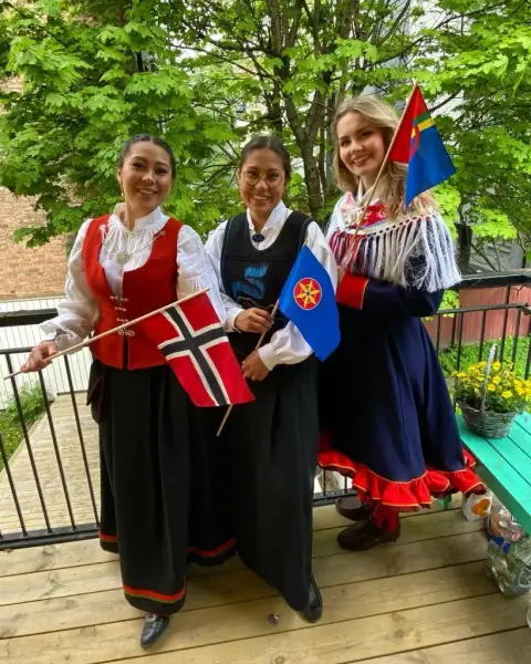 tre jenter i bunad med norsk, kvensk og samisk flagg